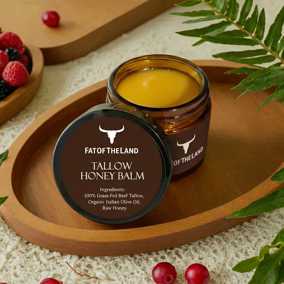 Jar of Tallow Honey Balm from FAT OF THE LAND on a wooden tray with berries and leaves.